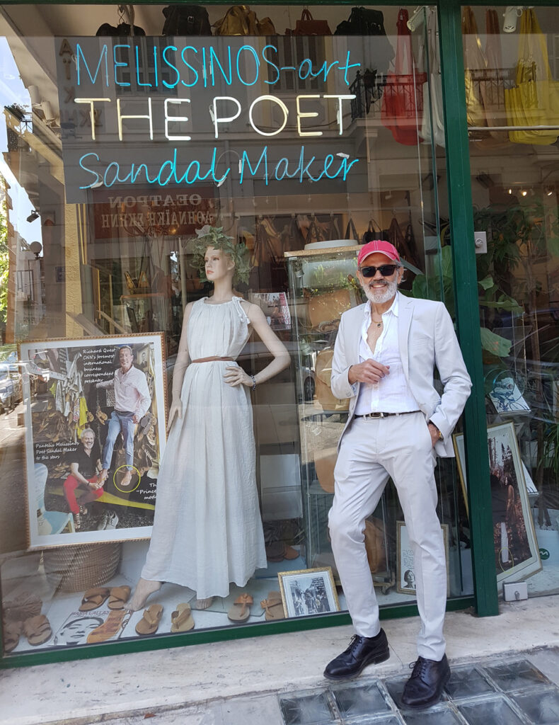 Pantelis Melissinos, "Poet Sandal Maker to the Stars", leaning against the display window of his sandal workshop & art gallery, in the Acropolis museum Area.